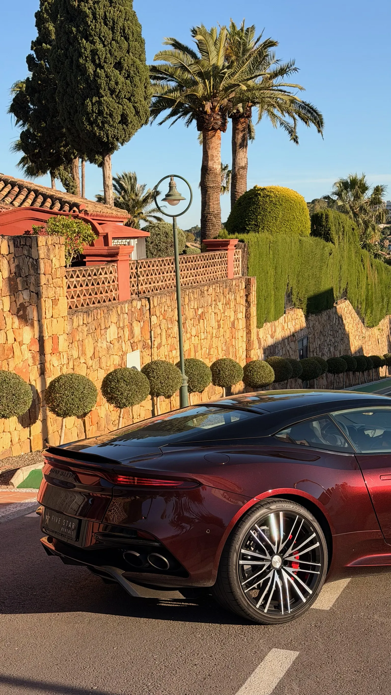 Rear side profile of the Divine Red Aston Martin DBS Superleggera with integrated boot spoiler, 21-inch Y-Spoke wheel and 305/30 Pirelli P Zero tyre