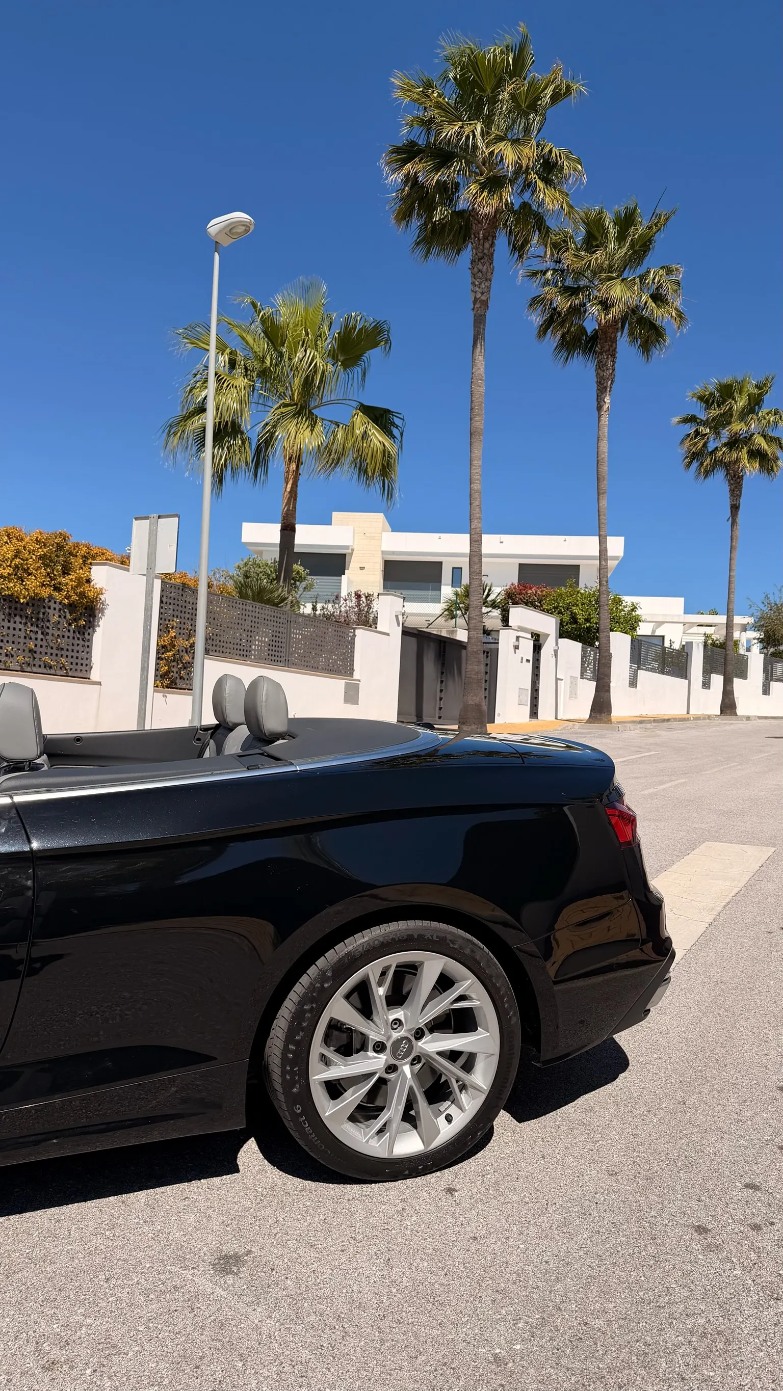 Vista trasera 3/4 del Audi A5 Cabriolet negro con llanta 5 radios dobles de 18 pulgadas y palmeras de Marbella
