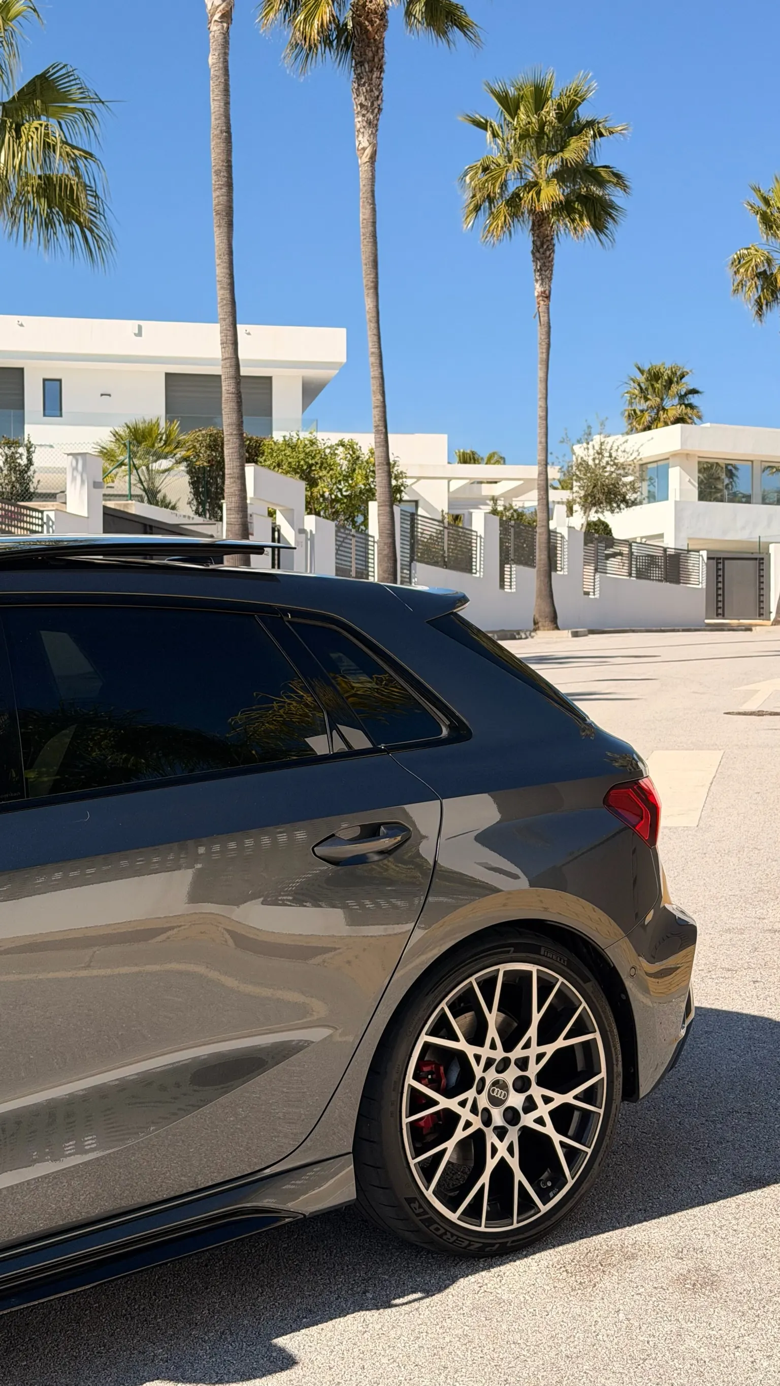 Rear side profile of the Audi RS3 Sportback with close-up rotor wheel and modern Marbella villas in background