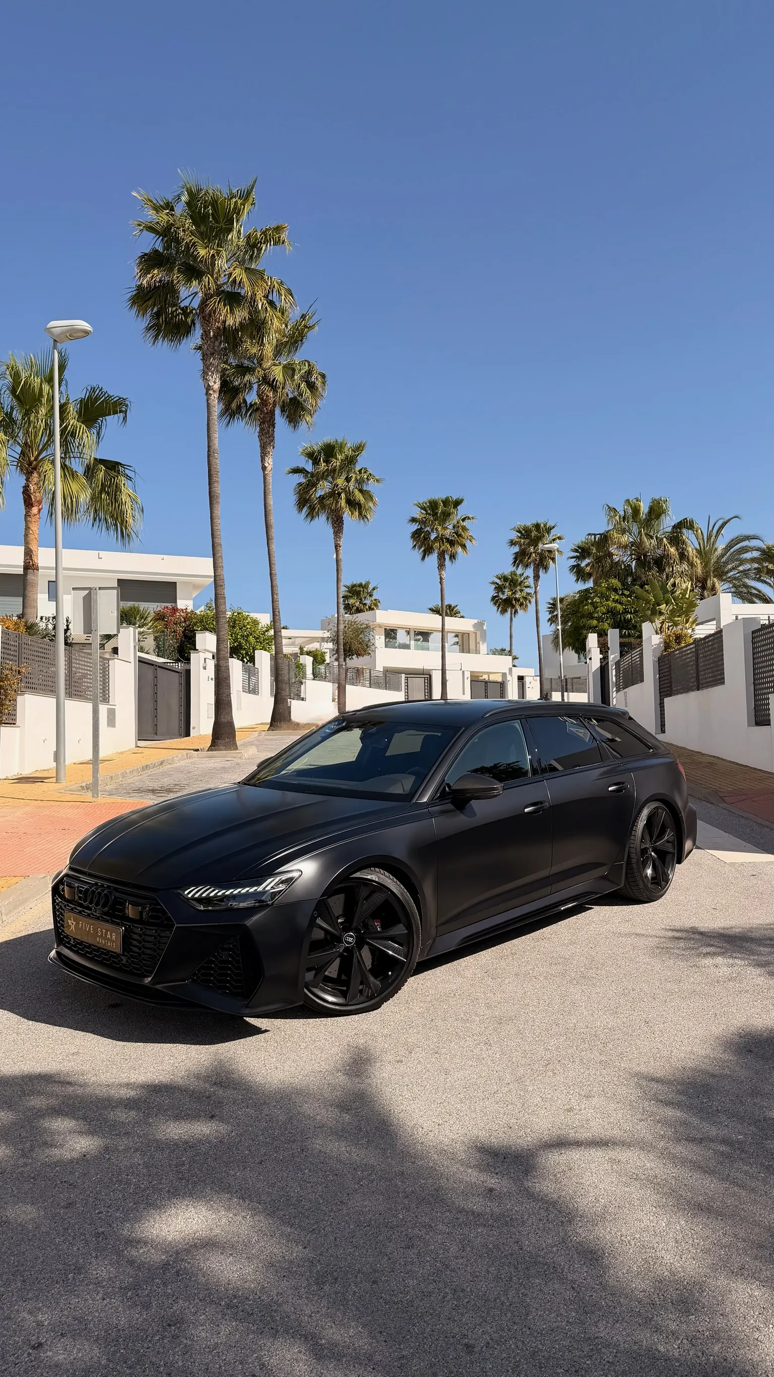 Audi RS6 Avant Performance in Mythos Black, front three-quarter view with Five Star Rentals plate and Marbella palm trees