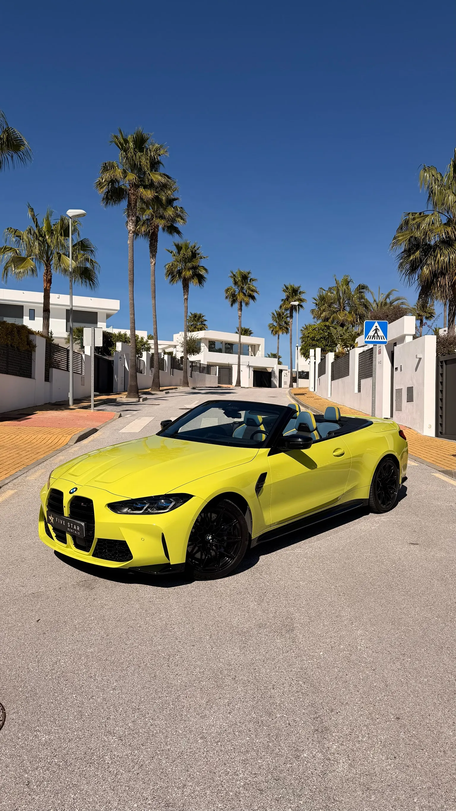 BMW M4 Competition Cabriolet São Paulo Yellow con capota abierta, vista 3/4 delantera con matrícula Five Star Rentals en una calle de Marbella