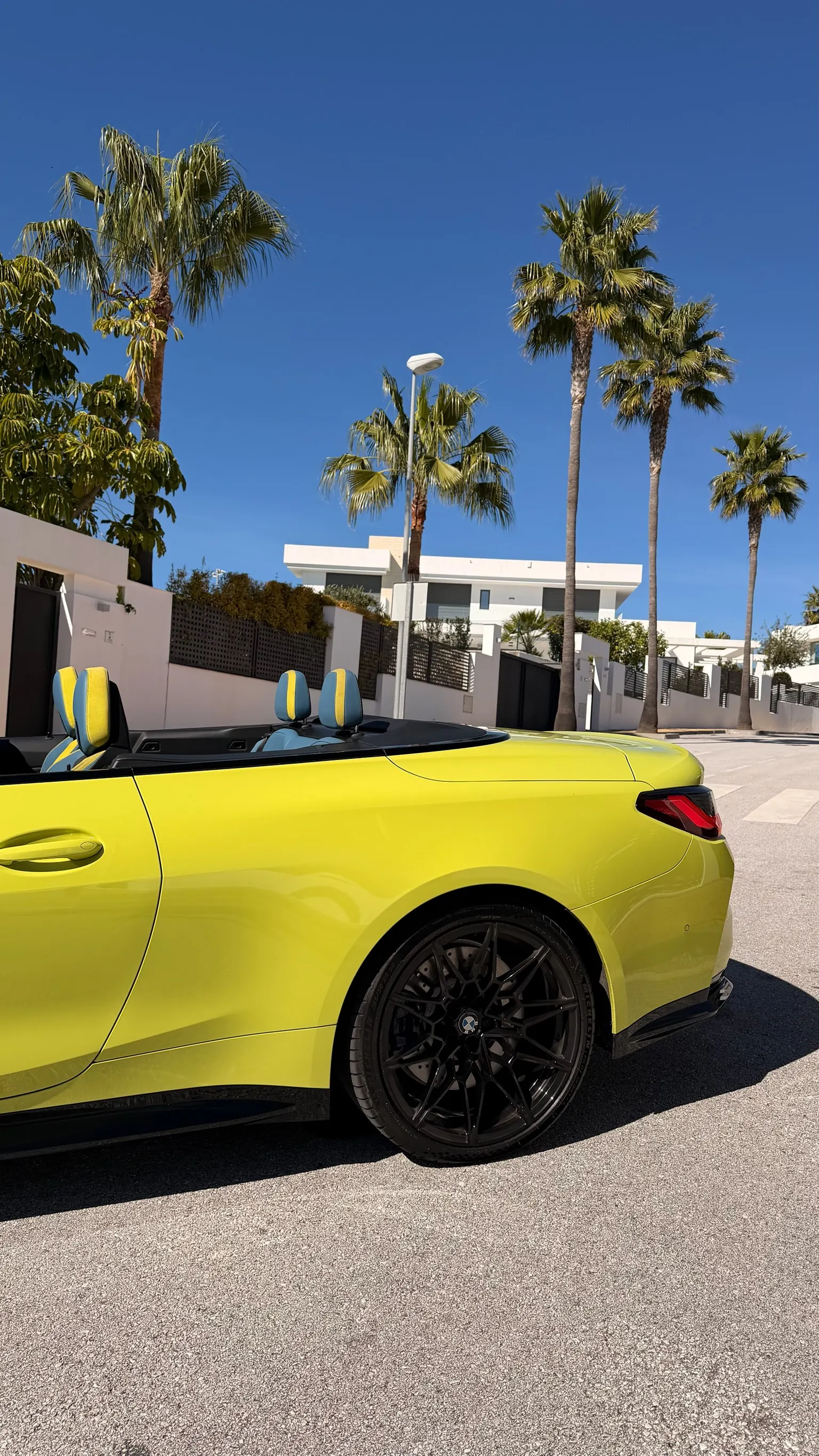 Vista trasera 3/4 del BMW M4 Cabriolet amarillo con llanta M negra e interior de cuero azul y amarillo BMW Individual visible
