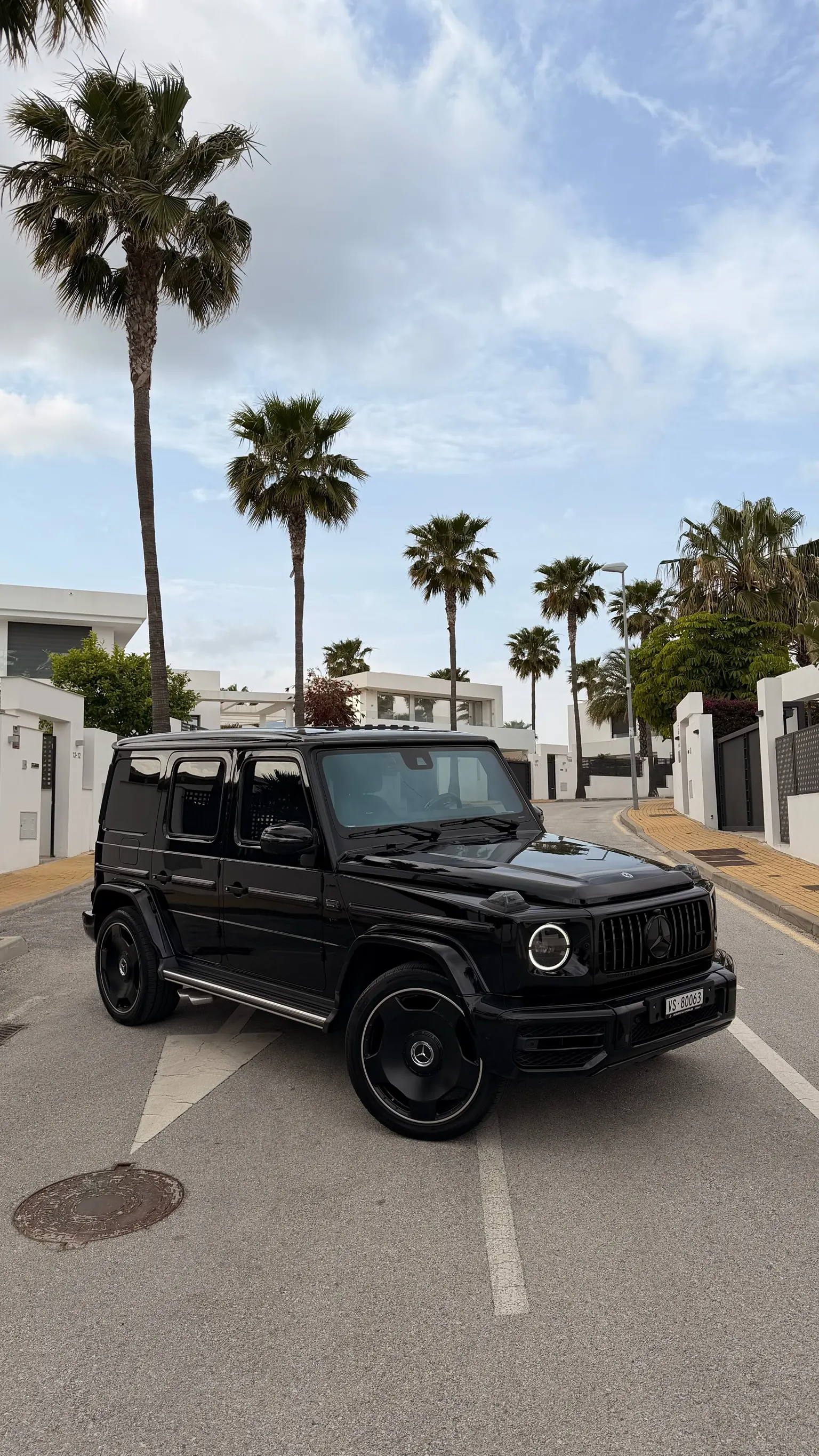 Mercedes-AMG G63 in Obsidian Black, front three-quarter view with Night package Panamericana grille, 22-inch black AMG wheels and Marbella palm trees