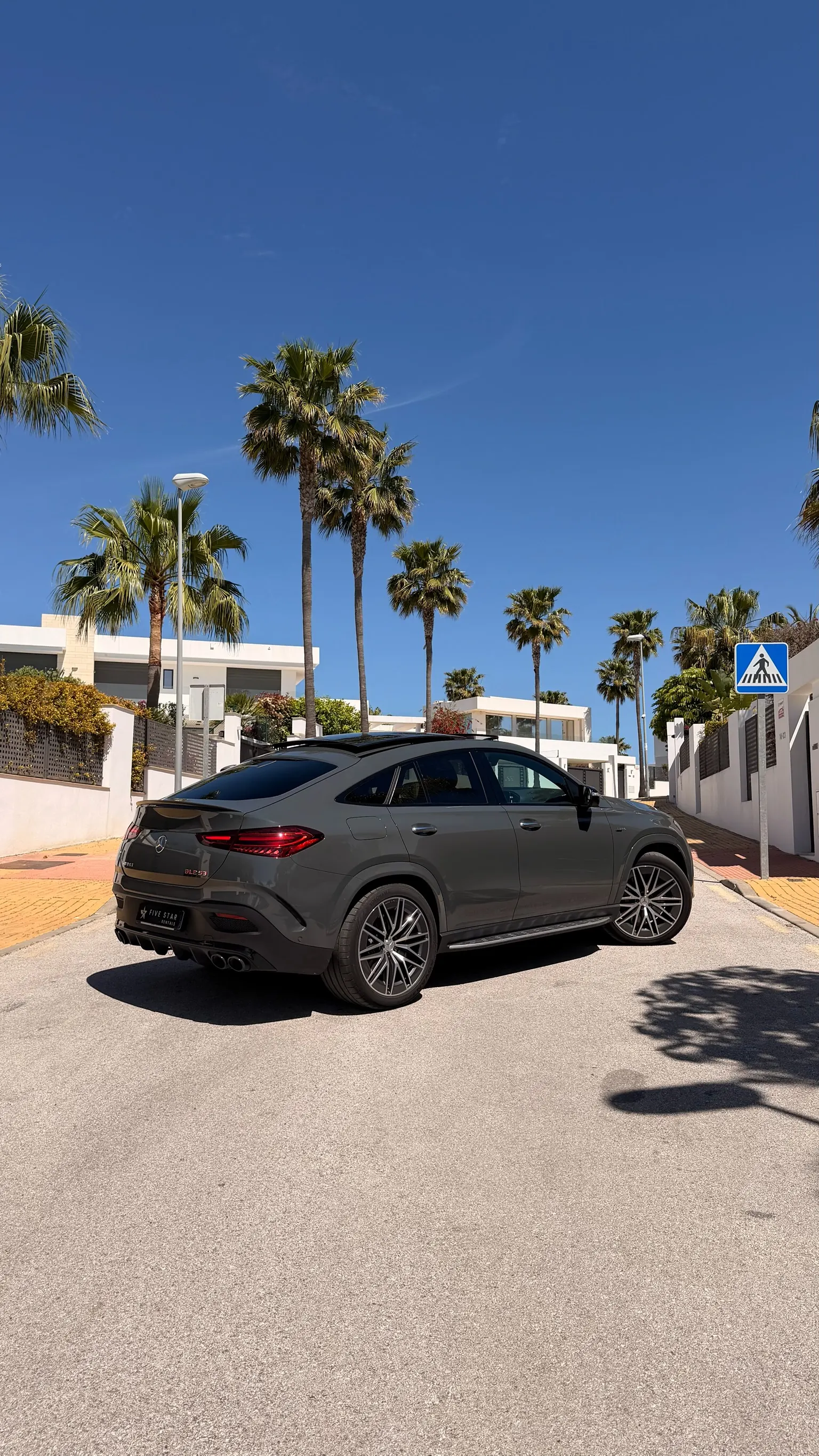 Rear three-quarter view of the Selenite Grey Mercedes-AMG GLE 53 Coupé with sloping coupé roofline, quad exhaust and 22-inch AMG wheel