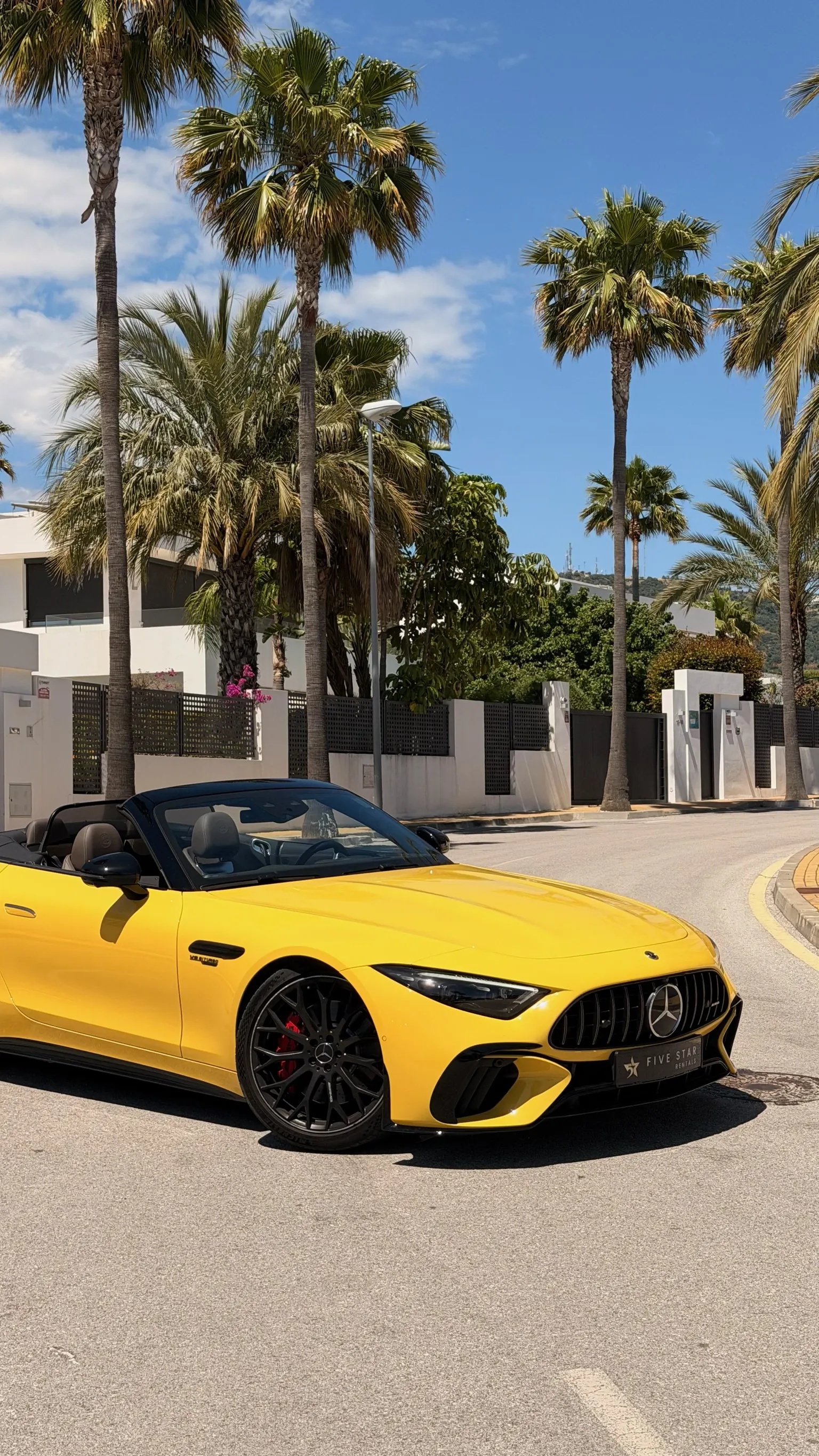 Vista 3/4 frontal de cerca del Mercedes-AMG SL 55 Sun Yellow con matrícula Five Star Rentals, insignia V8 BITURBO en aleta, llantas en aspa negro mate y pinzas Brembo rojas