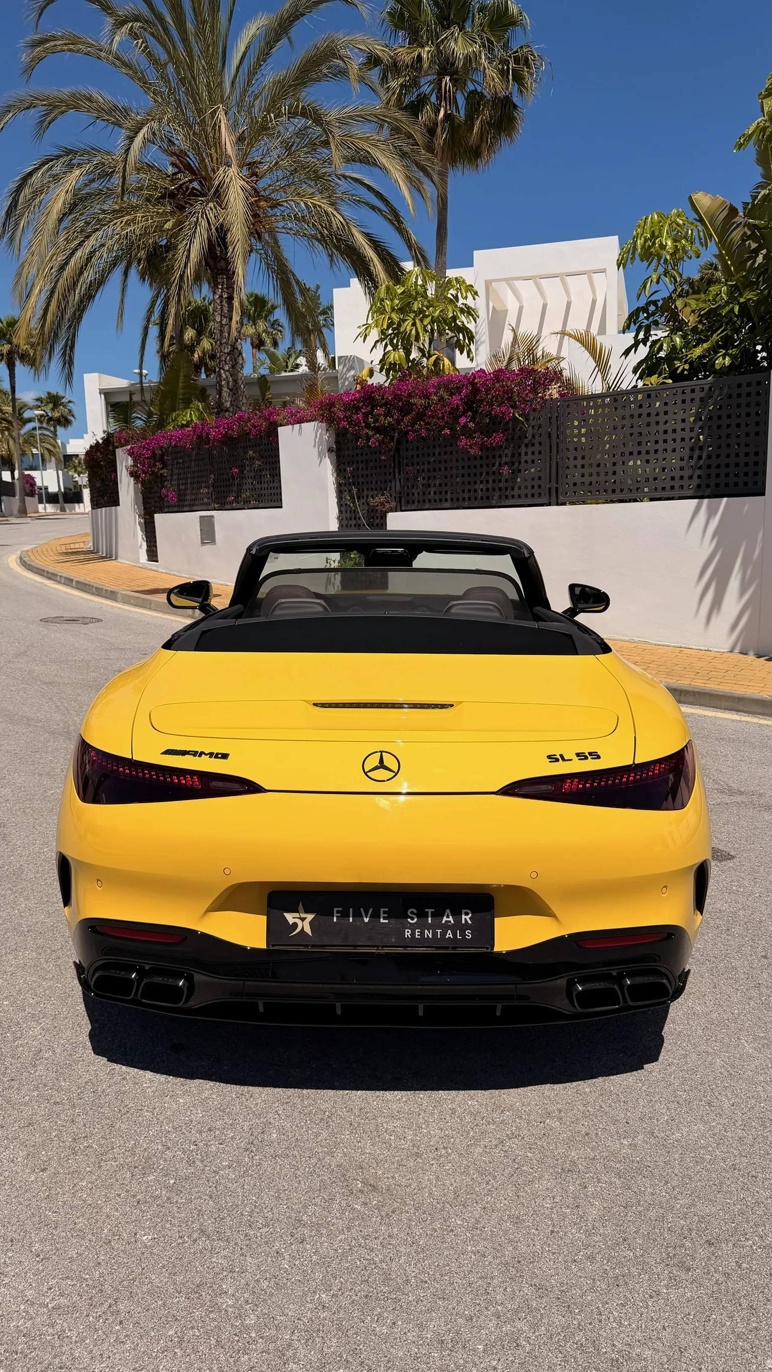 Vista trasera centrada del Mercedes-AMG SL 55 4MATIC+ Sun Yellow con matrícula Five Star Rentals, insignias AMG y SL 55, y doble salida de escape negra integrada en el difusor