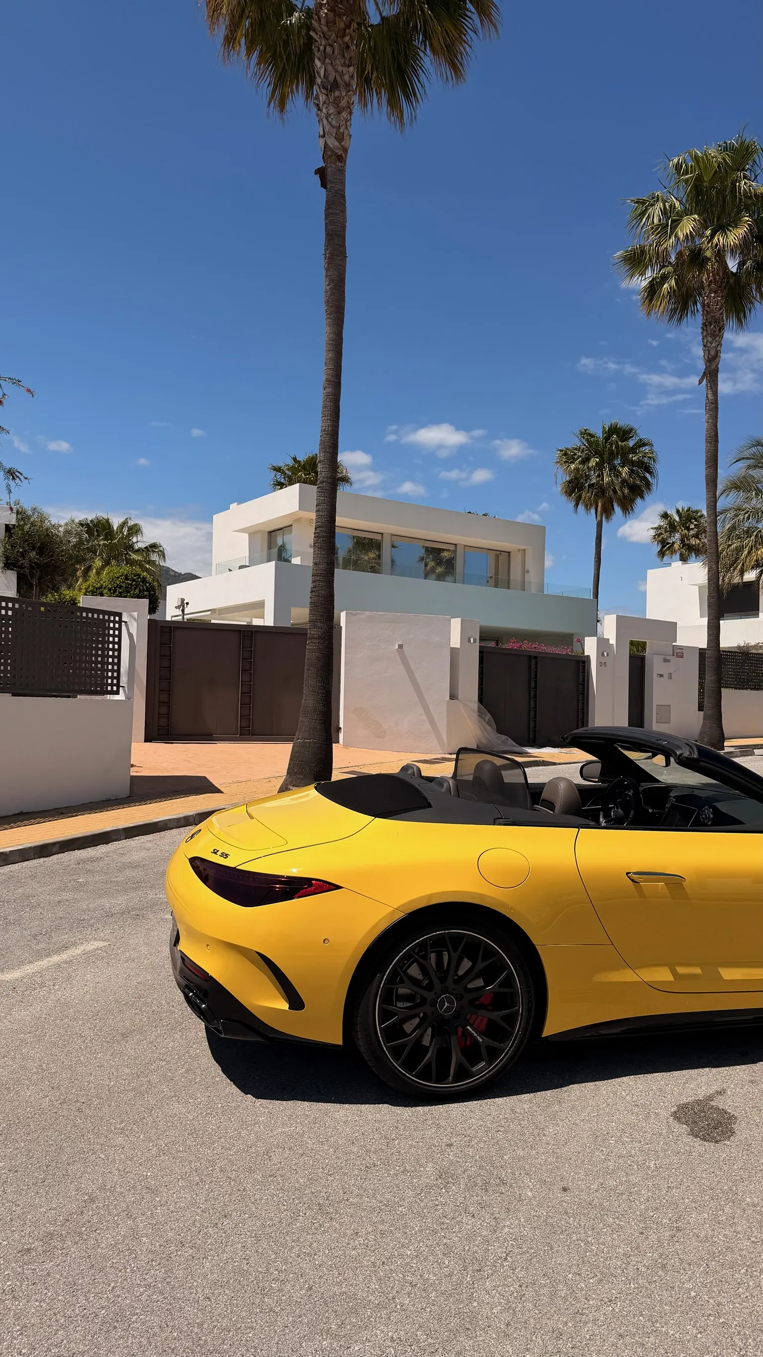 Perfil trasero del Mercedes-AMG SL 55 Sun Yellow con capota abierta, insignia SL 55 en maletero, llantas de 21 pulgadas negro mate y pinzas Brembo rojas