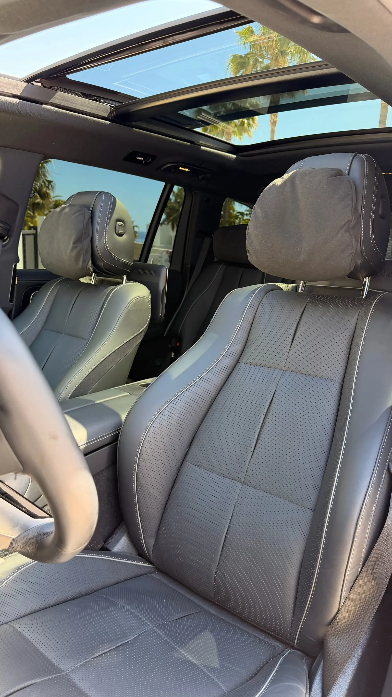 Mercedes-Benz GLS 580 front seats in perforated black Nappa leather with contrast white stitching, panoramic roof open onto Marbella palm trees