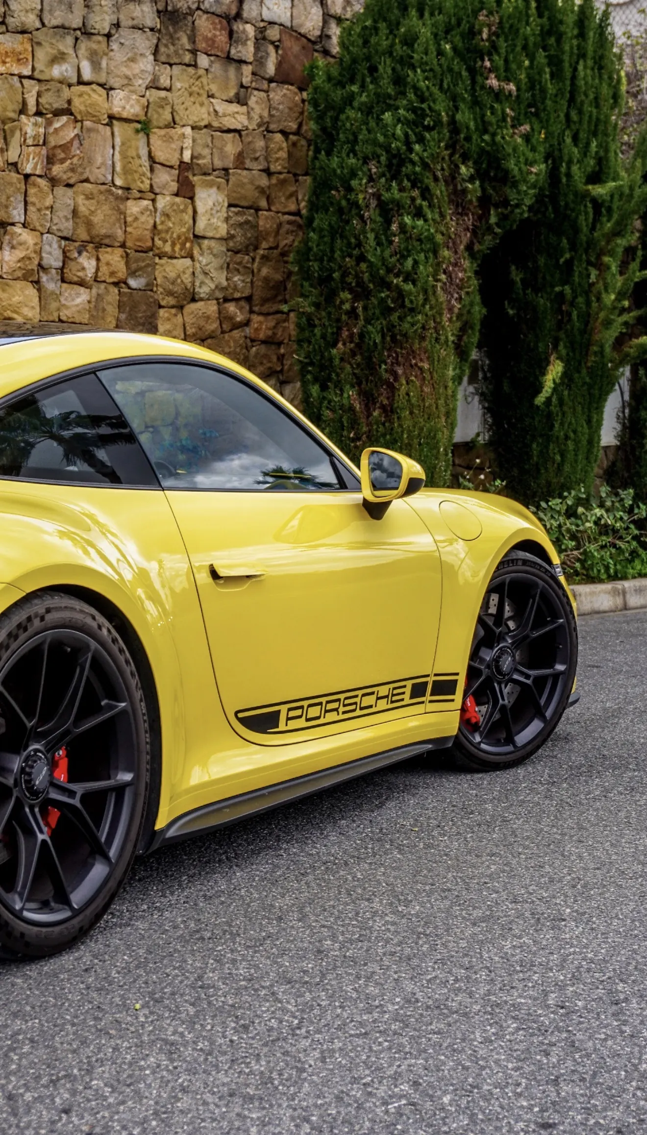 Perfil lateral del Porsche 911 GT3 992 Racing Yellow con calcomanías PORSCHE negras en los faldones, llantas forjadas negro mate y pinzas de freno rojas