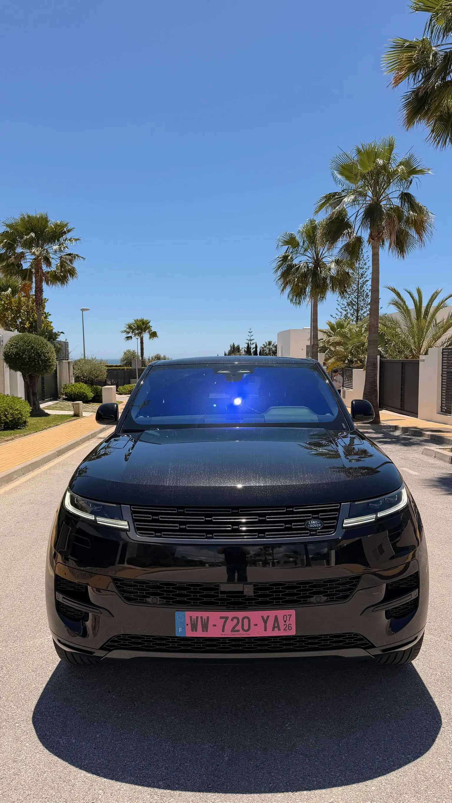 Vista frontal centrada del Range Rover Sport P460e negro Santorini con parrilla negra, faros LED y paragolpes deportivo bajo palmeras de Marbella